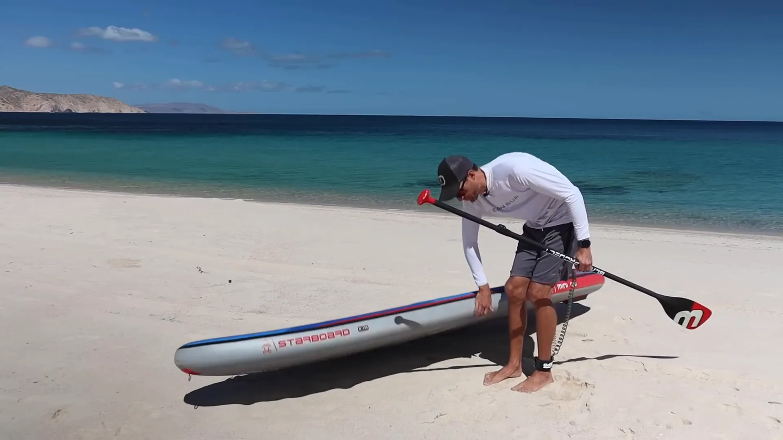 Person carrying paddle board into knee-deep water